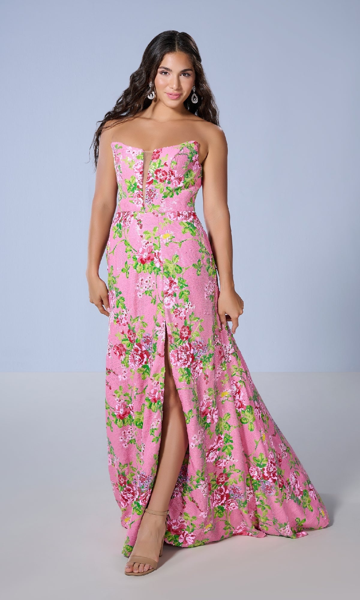 A woman models the Long Prom Dress: Tiffany 16143, a strapless floral gown with pink accents and a front slit, standing before a plain light blue background.